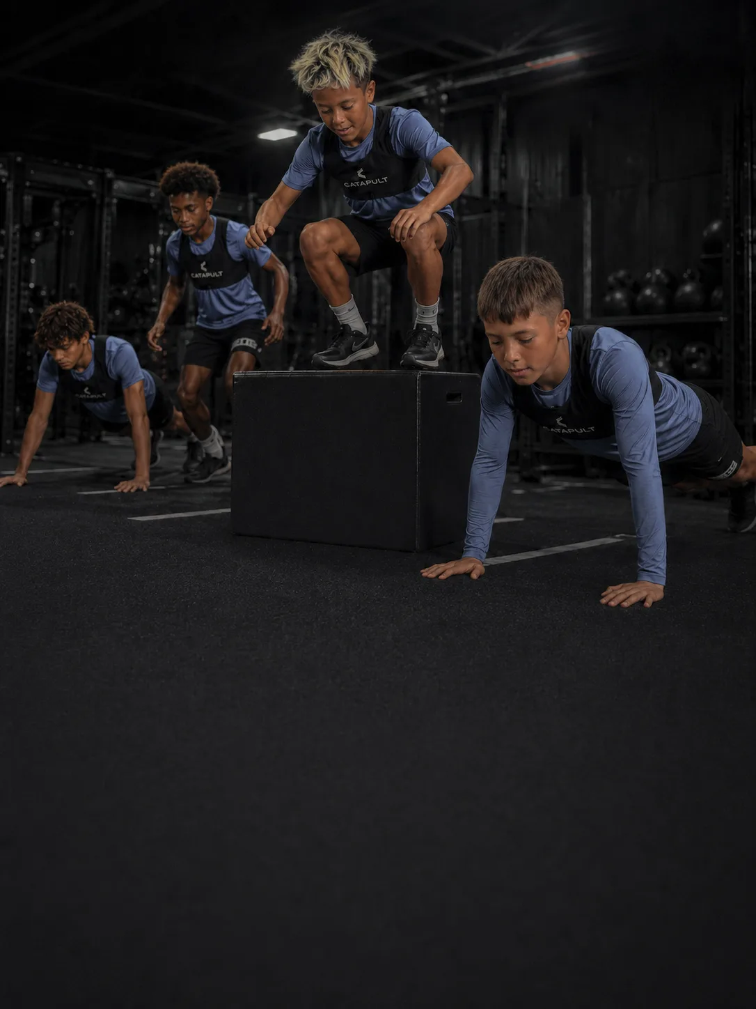 Young athletes in Catapult gear doing box jumps in a dark gym