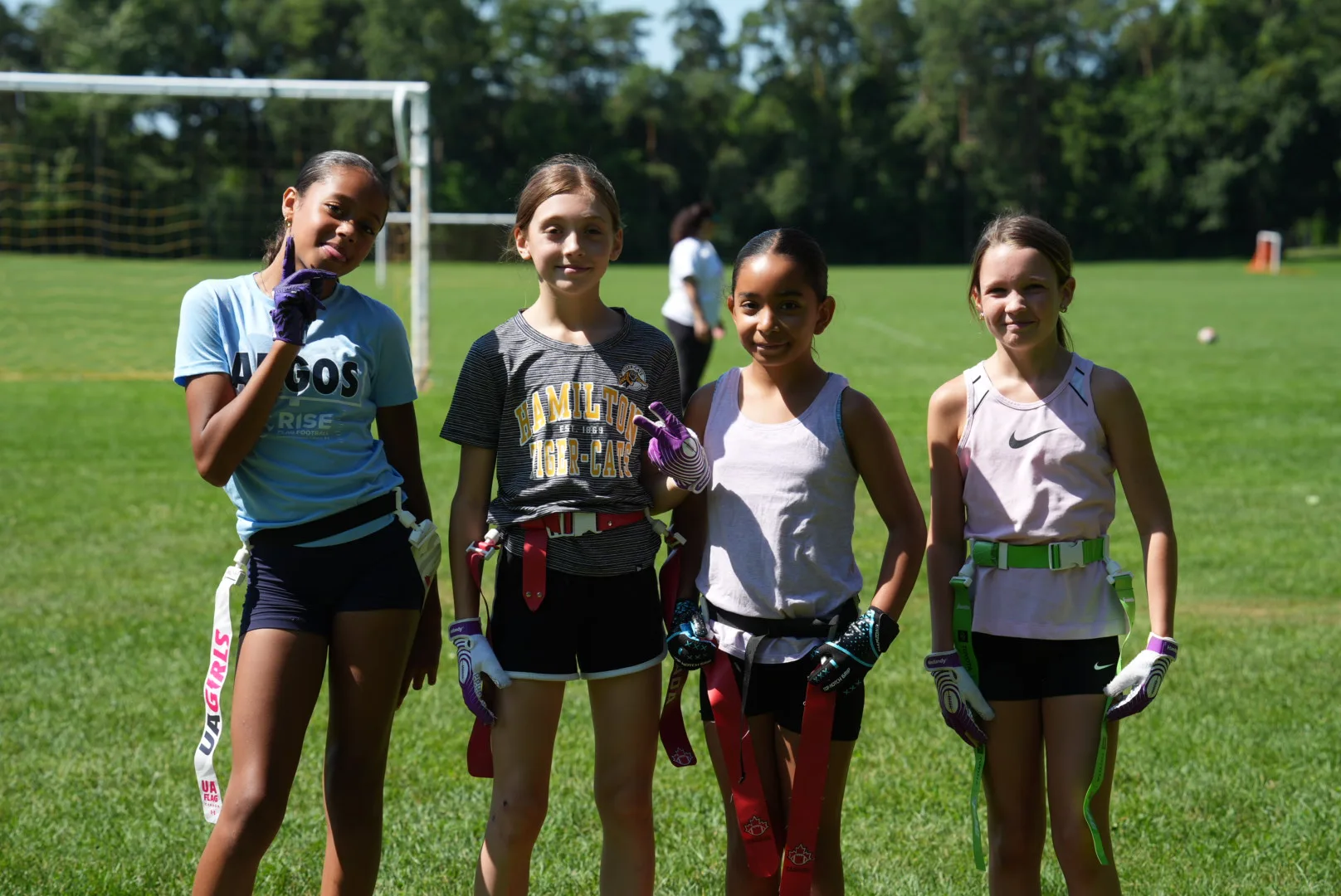 Four young athletes in flag football gear smiling together on the field